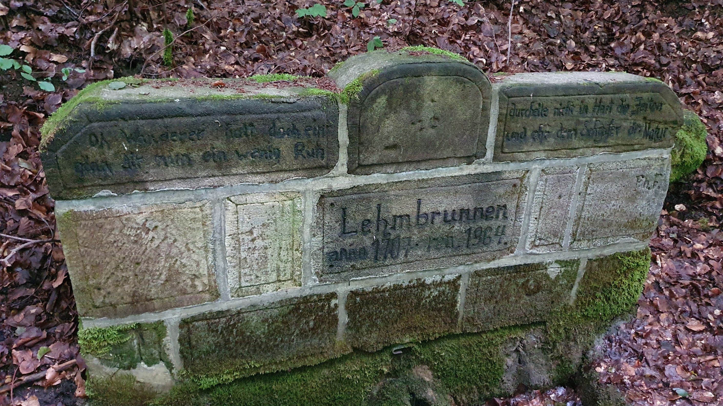 Lehm(en)brunnen nordwestlich von Oberlangheim. Die Schlusssteine der Quellfassung sind mit der Inschrift „Oh Wanderer halt doch ein I gönn dir nun ein wenig Ruh I durcheile nicht in Hast die Zeiten I und ehre den Schöpfer der Natur“ als ein Zeichen für den Nutzungszweck der Quelle und des Brunnens versehen. Zu sehen ist auch das Datum, wann der Brunnen gefasst/erbaut (1707) und zuletzt renoviert wurde (1964).
Aufnahme: 2023 David Marvin Klotz - Otto-Friedrich-Universität Bamberg, Creative-Commons-Lizenz by-nc-nd-4.0